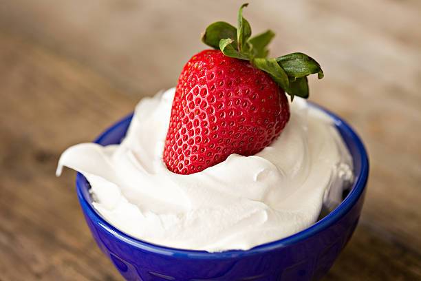 A close up shot of a red strawberry dipped in white whipping cream in a small blue bowl. The perfect dessert.