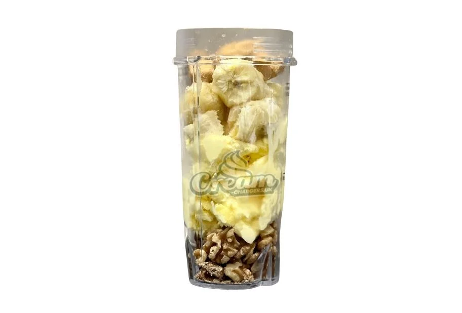 Ingredients for a high calorie milkshake for weight gain, including sliced bananas, peanut butter, ice cream and walnuts, layered in a clear ninja bullet cup