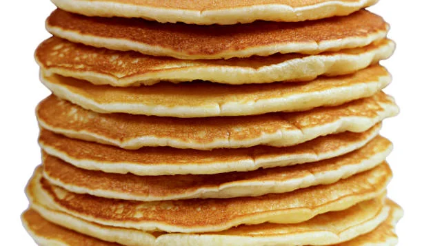 A tall stack of bulking breakfast pancakes on a white background