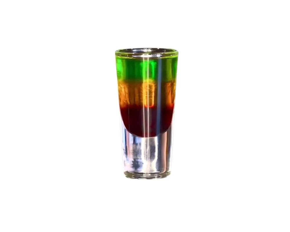 A tall shot glass containing a layered drink that creates a visual effect similar to a traffic light, with distinct layers of green, amber, and red, set against a plain background that accentuates the vibrant colours